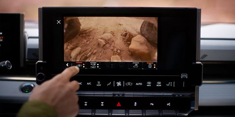 
Driver pointing at an infotainment screen displaying a rocky terrain view from an underbody camera.