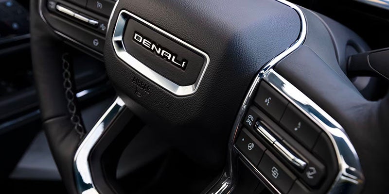 
Close-up of a GMC Denali steering wheel showing the 'DENALI' badge and control buttons.